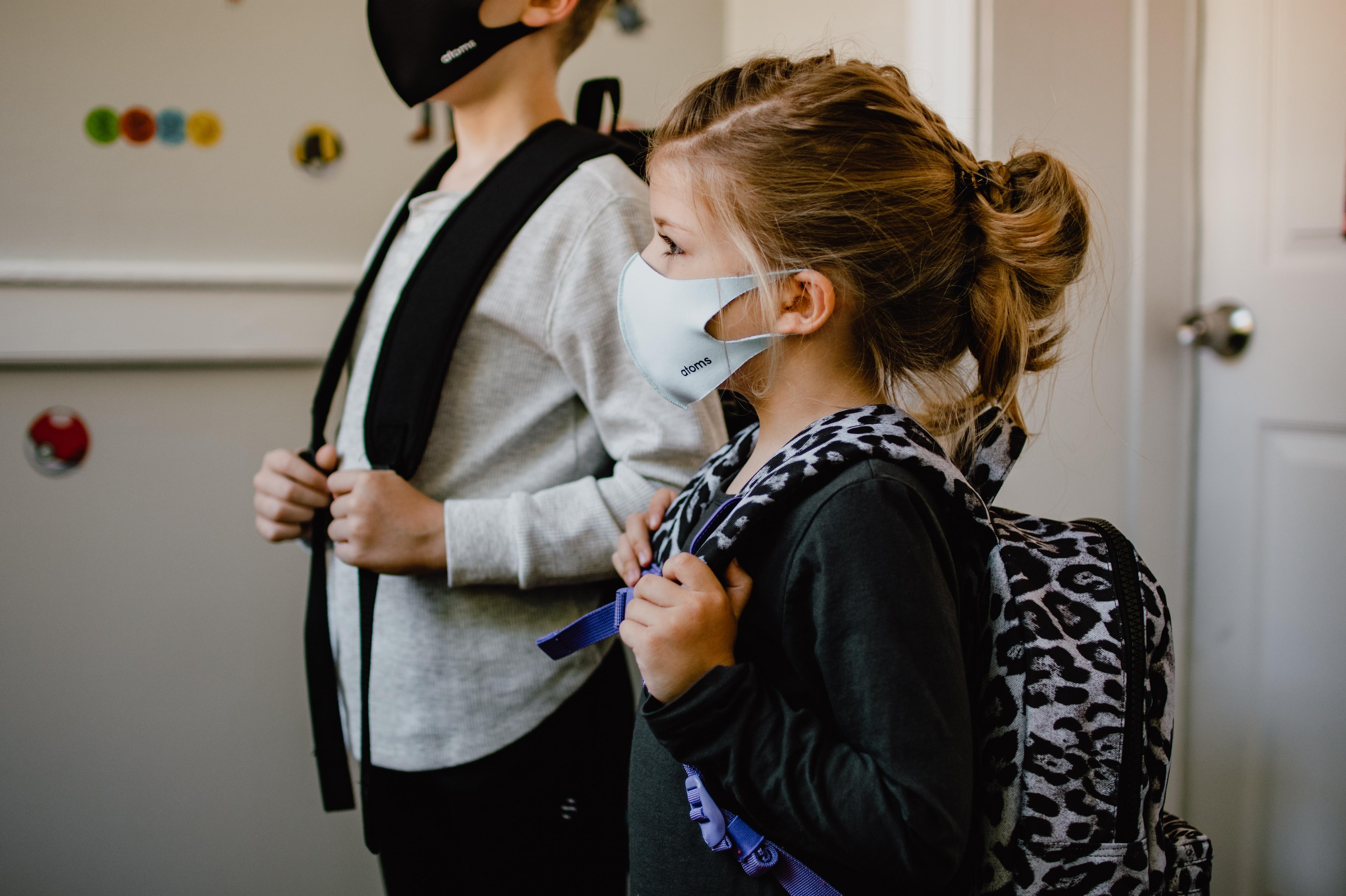 Two children weariing a mask and carrying backpacks